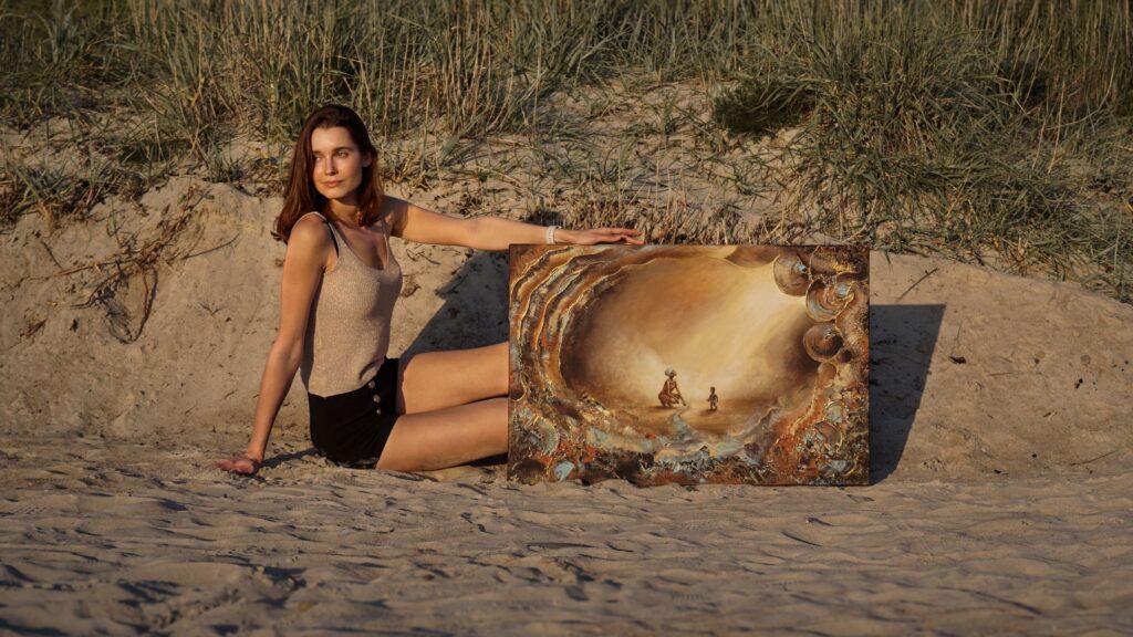 Artist Isabel Silla holding her original textured painting "Del Sol" on the beach at golden hour, showcasing earthy tones, gold accents, and natural light