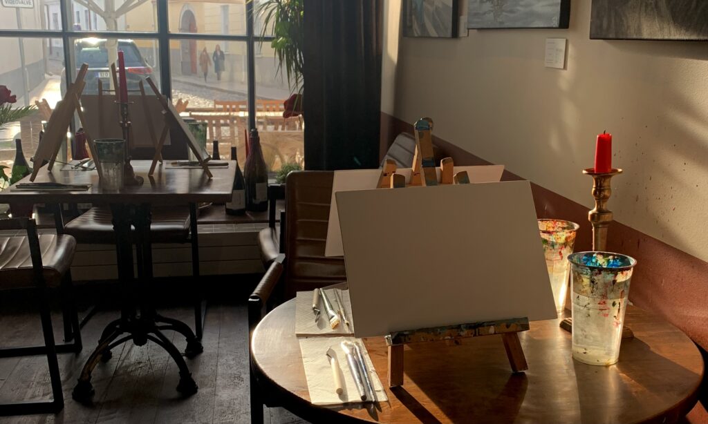 Table setup for Sip & Paint evening at Toro Wine Bar in Tallinn, featuring easels, brushes, and candles in a cozy, sunlit setting