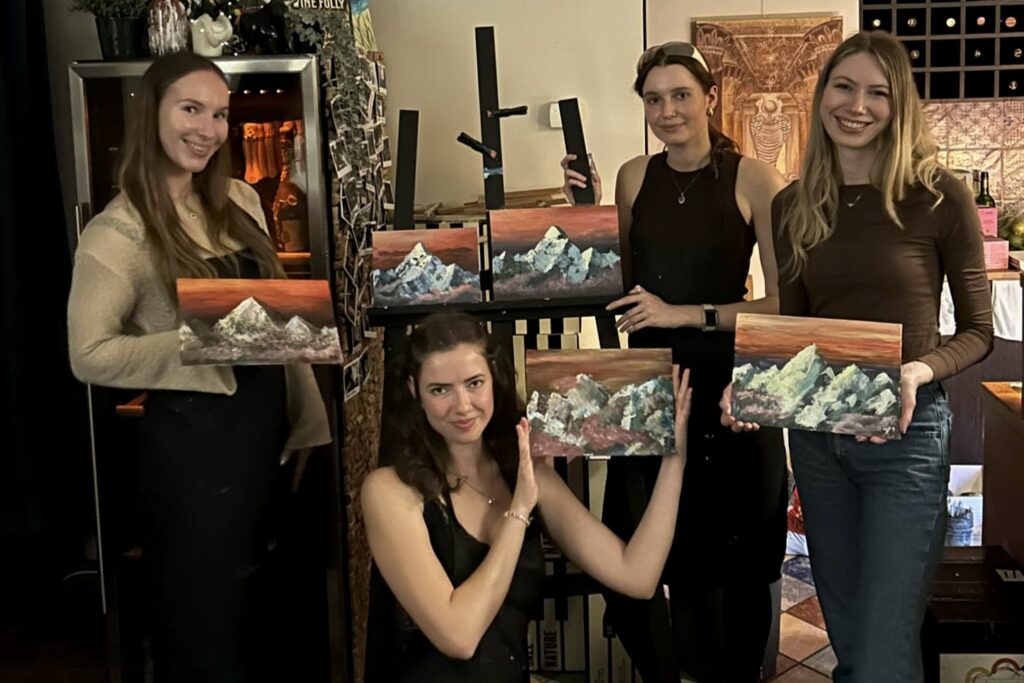 Group photo of Sip & Paint attendees in Tallinn holding up their completed mountain paintings at Toro Wine Bar